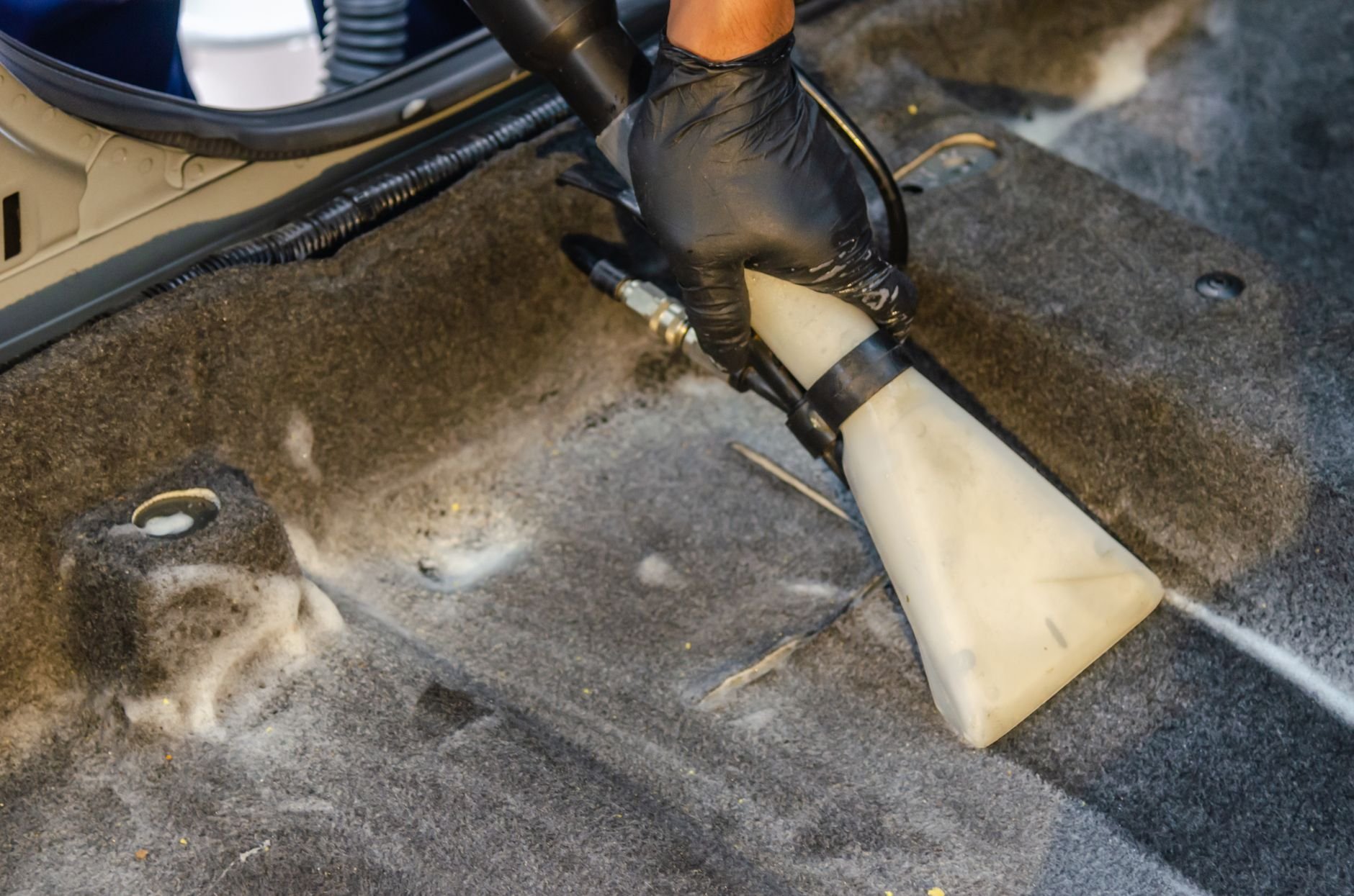 A hand using a high-power portable vacuum to clean a car interior carpet