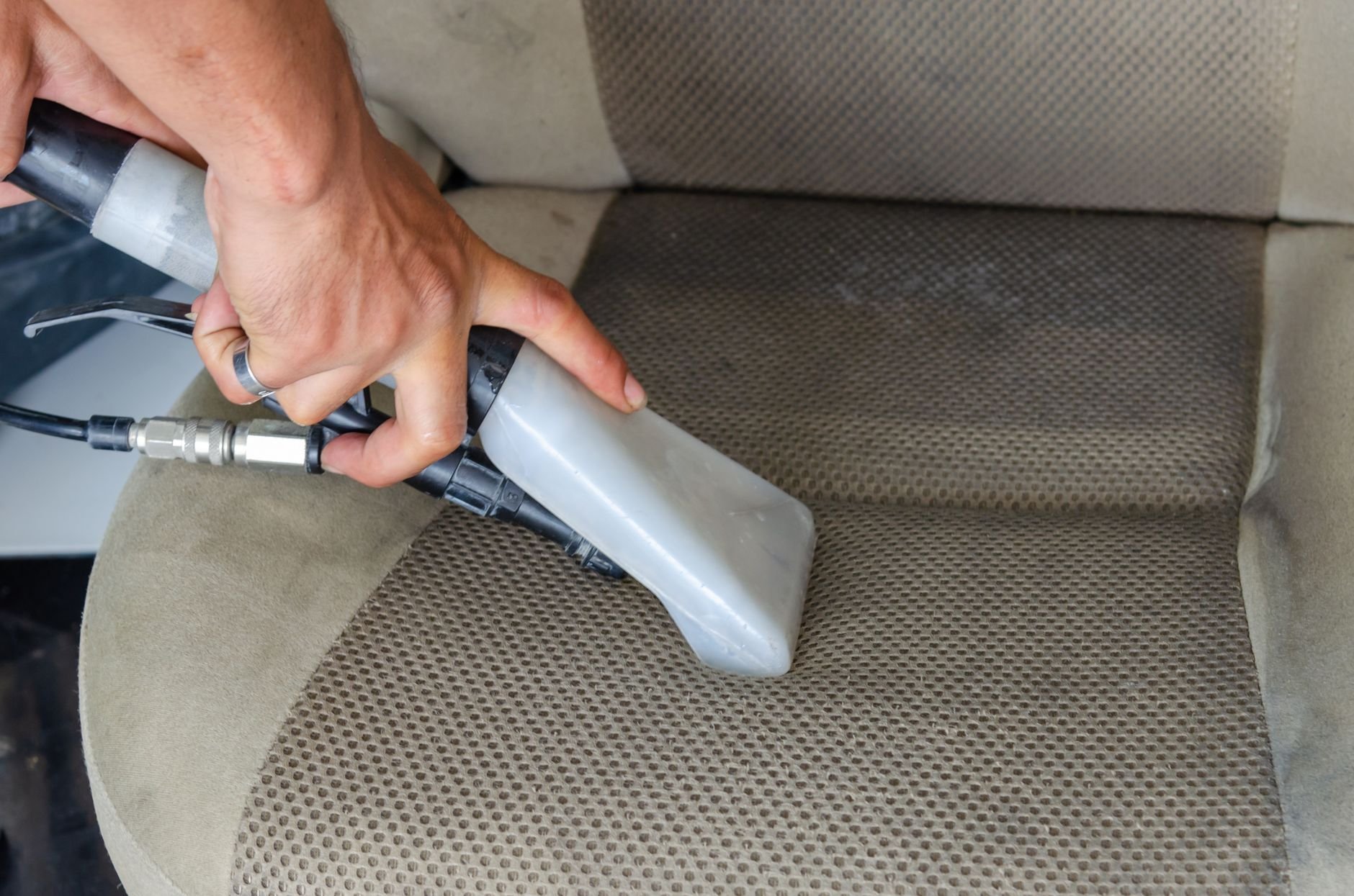 Hands using a vacuum nozzle to deeply clean a fabric car seat, removing dirt and stains